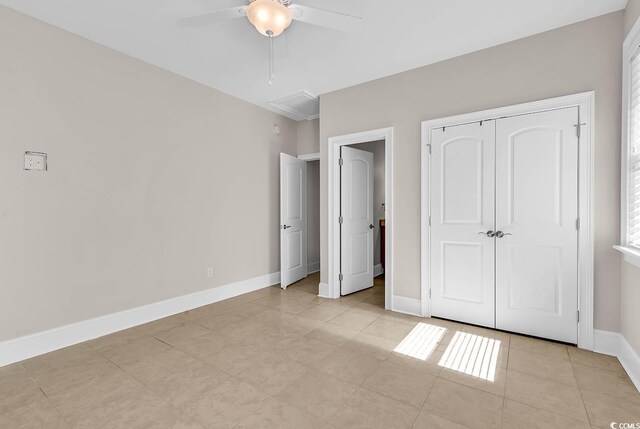 unfurnished bedroom with attic access, light tile patterned floors, a closet, ceiling fan, and baseboards