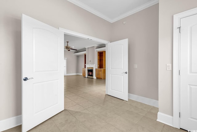 empty room featuring a warm lit fireplace, baseboards, light tile patterned flooring, ornamental molding, and a ceiling fan