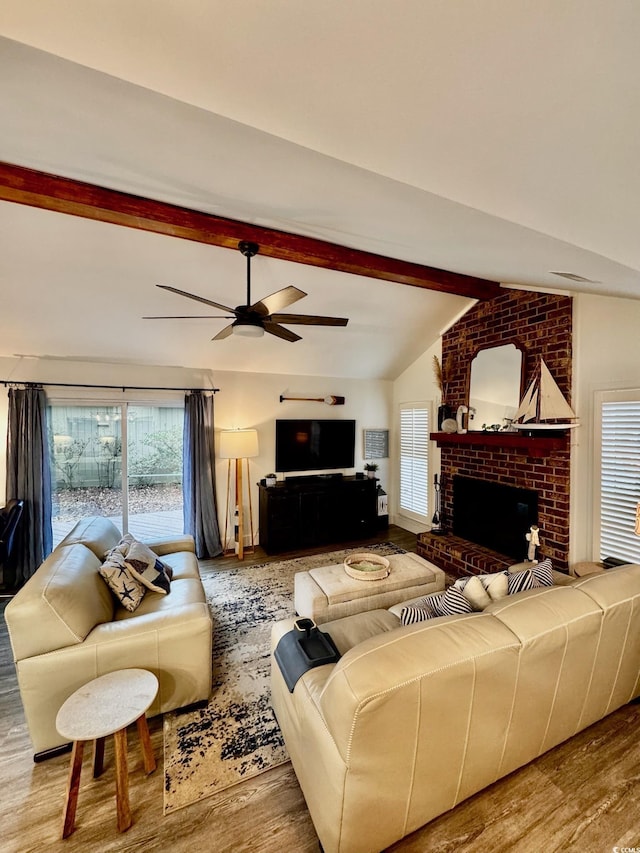 living area featuring a ceiling fan, vaulted ceiling with beams, a fireplace, and wood finished floors