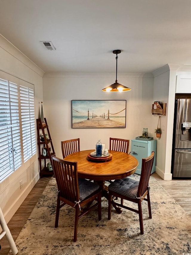 dining space featuring light wood-style flooring, crown molding, baseboards, and visible vents