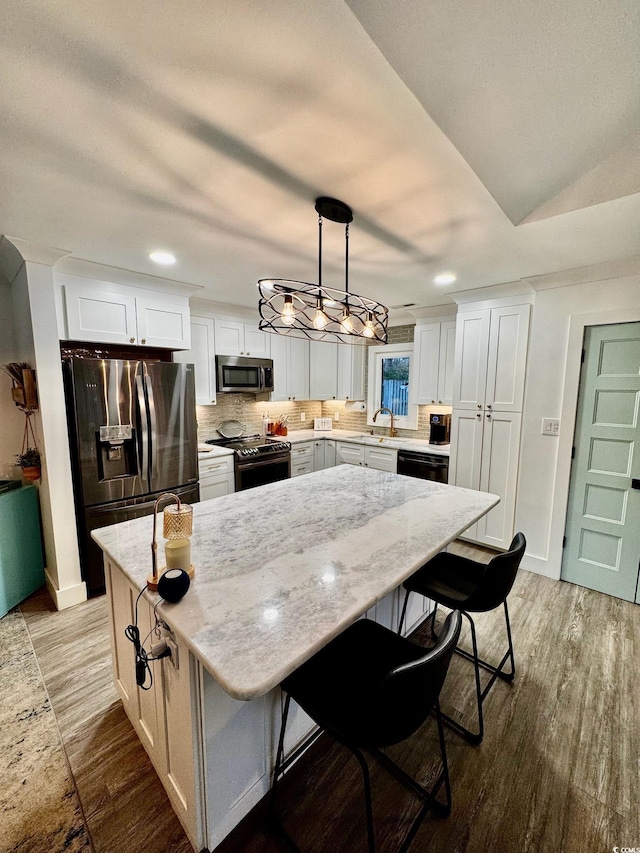 kitchen featuring light stone counters, backsplash, a kitchen island, wood finished floors, and stainless steel appliances