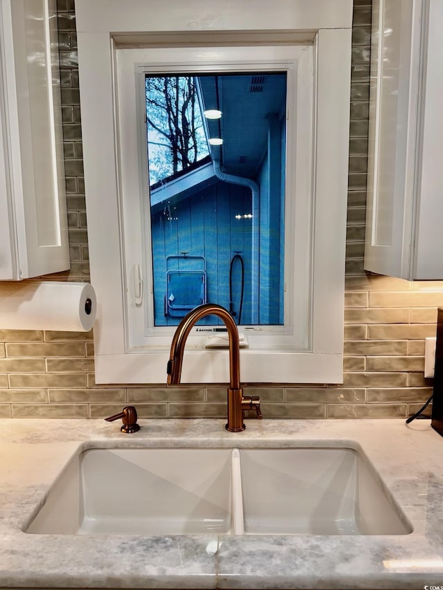 room details featuring white cabinets, a sink, tasteful backsplash, and light stone countertops