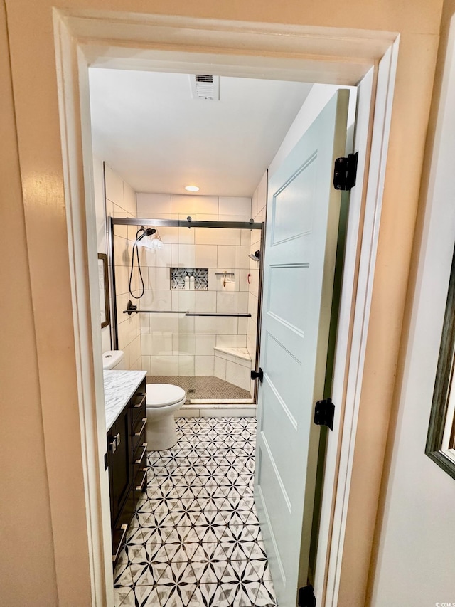 full bathroom with a stall shower, visible vents, toilet, and vanity