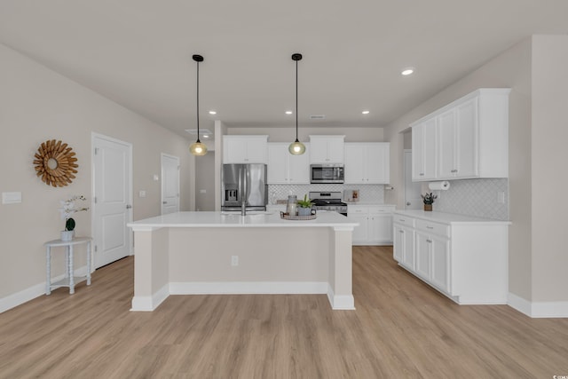 kitchen featuring appliances with stainless steel finishes, light wood-type flooring, backsplash, light countertops, and a kitchen island with sink