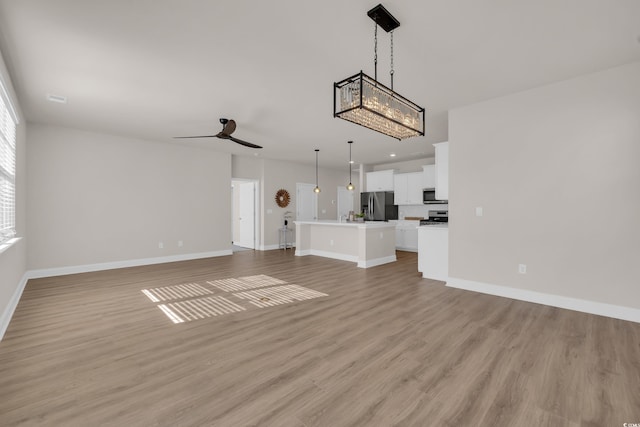 unfurnished living room featuring baseboards, light wood-style floors, a ceiling fan, recessed lighting, and a chandelier