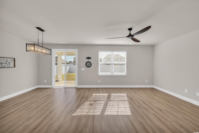 unfurnished room with ceiling fan, wood finished floors, baseboards, and a chandelier
