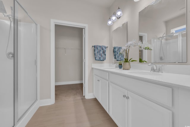 bathroom featuring a shower stall, a walk in closet, baseboards, and double vanity