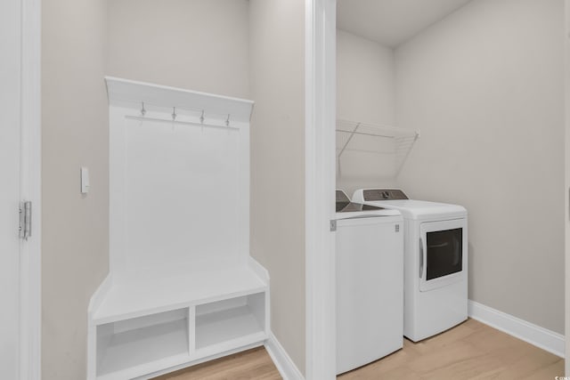 clothes washing area with light wood-style flooring, washing machine and dryer, and baseboards