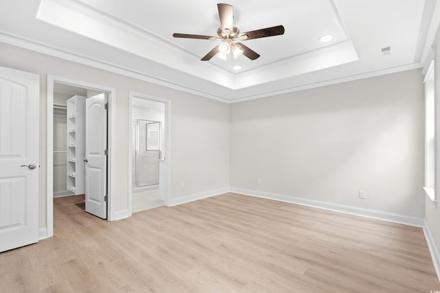 unfurnished bedroom featuring a walk in closet, a tray ceiling, ornamental molding, light wood-style flooring, and recessed lighting