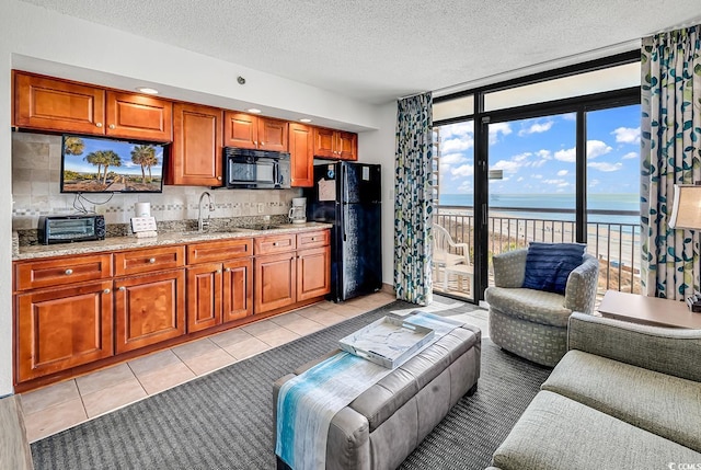 living room with expansive windows, light tile patterned floors, a water view, and a textured ceiling