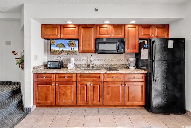 kitchen featuring light stone counters, brown cabinets, black appliances, and a sink