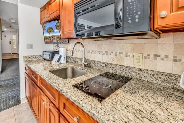 kitchen featuring backsplash, light stone countertops, brown cabinets, black appliances, and a sink
