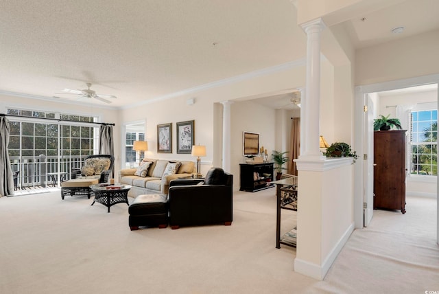 living room featuring decorative columns, light colored carpet, ceiling fan, and crown molding