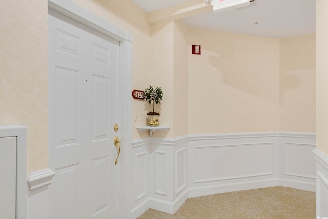 entryway featuring wainscoting, a decorative wall, and carpet floors