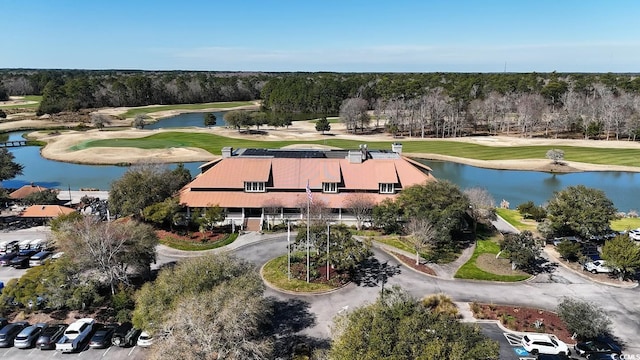 drone / aerial view of a golf course, a nearby body of water, and a tree filled landscape