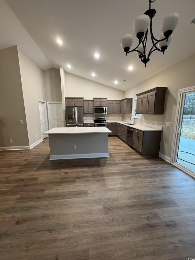kitchen with appliances with stainless steel finishes, light countertops, vaulted ceiling, a sink, and a center island