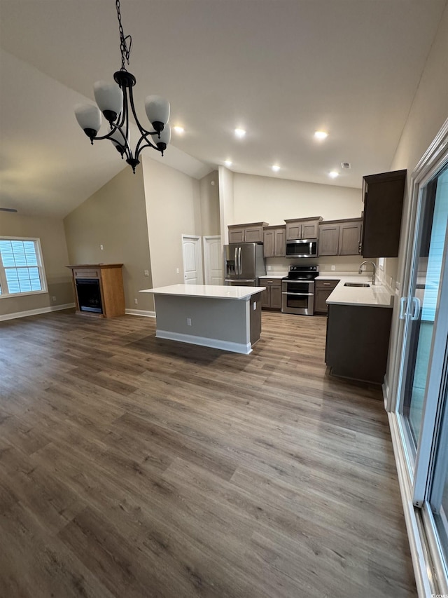 kitchen featuring appliances with stainless steel finishes, a kitchen island, vaulted ceiling, a sink, and open floor plan