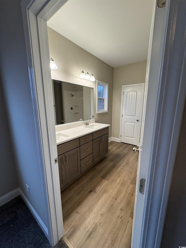 full bath with double vanity, a sink, wood finished floors, and baseboards