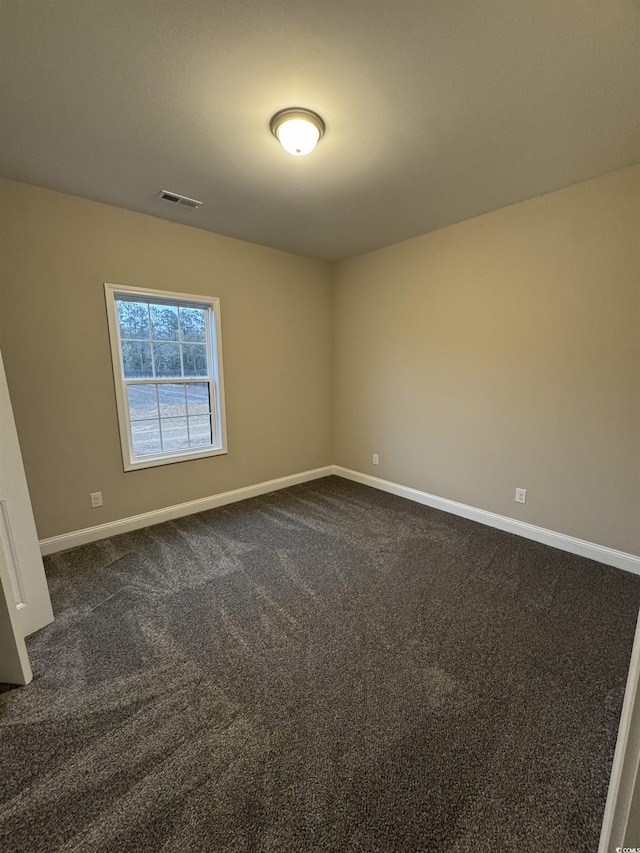 spare room featuring baseboards, visible vents, and dark colored carpet
