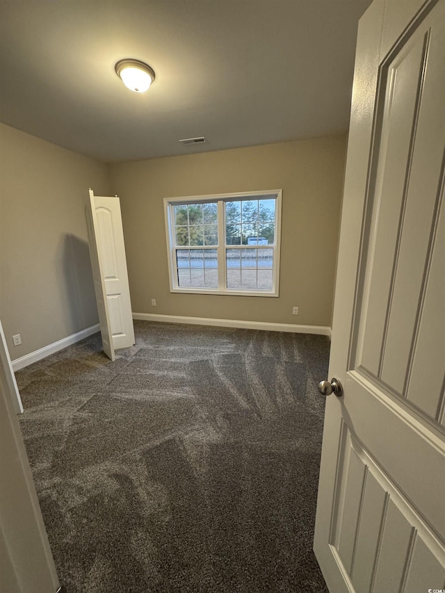 unfurnished bedroom with baseboards, dark colored carpet, and visible vents