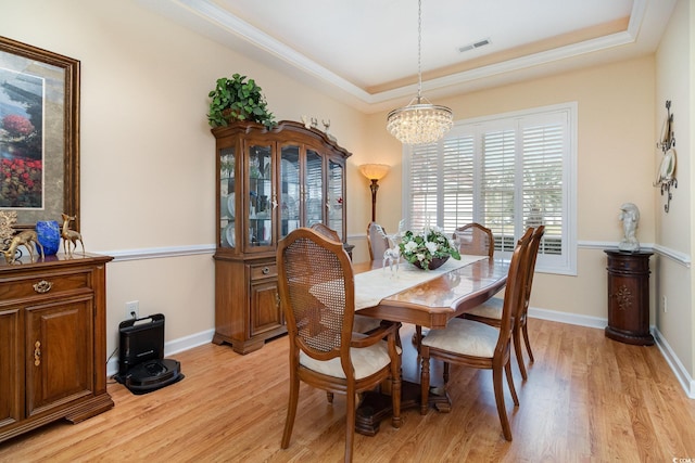 dining space with a tray ceiling, an inviting chandelier, light wood-style floors, and visible vents