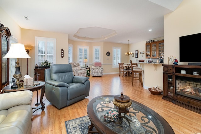 living room with recessed lighting, a notable chandelier, a tray ceiling, and light wood-type flooring