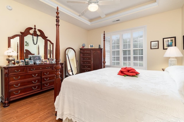 bedroom with wood finished floors, crown molding, visible vents, a raised ceiling, and ceiling fan