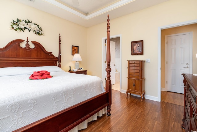 bedroom featuring ensuite bathroom, crown molding, dark wood-style floors, a raised ceiling, and baseboards