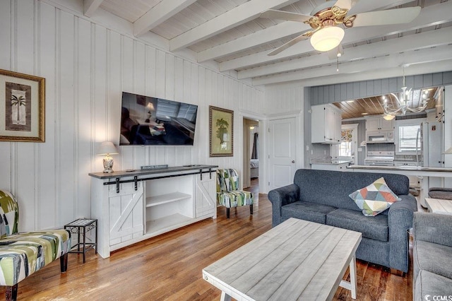 living area with beam ceiling, ceiling fan with notable chandelier, and wood finished floors