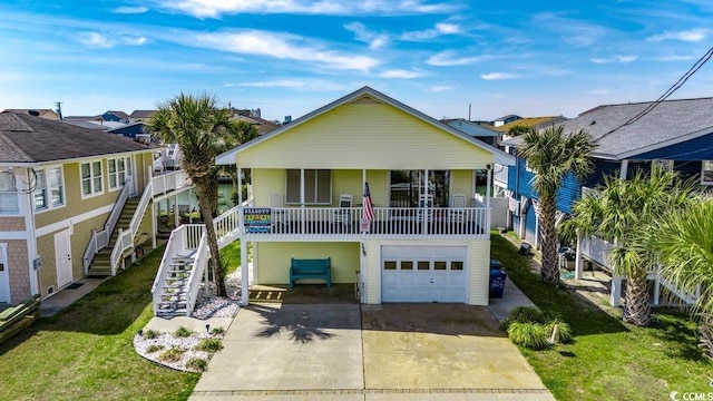 coastal inspired home with covered porch, a front yard, stairs, concrete driveway, and an attached garage