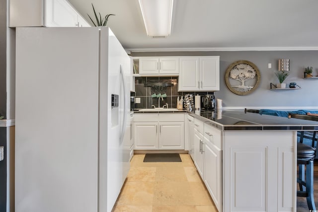 kitchen with a peninsula, white cabinets, dark countertops, and white fridge with ice dispenser