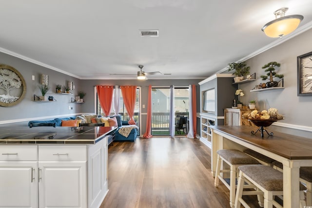 kitchen with tile countertops, white cabinets, wood finished floors, and ornamental molding