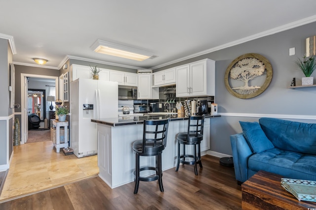 kitchen featuring dark countertops, a peninsula, white fridge with ice dispenser, white cabinetry, and stainless steel microwave
