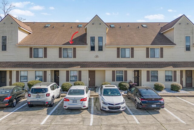 view of property with roof with shingles and uncovered parking
