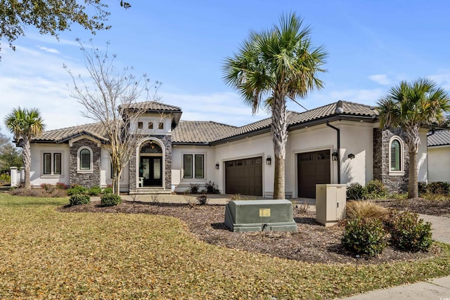 mediterranean / spanish house with stucco siding, stone siding, an attached garage, a front yard, and a tiled roof