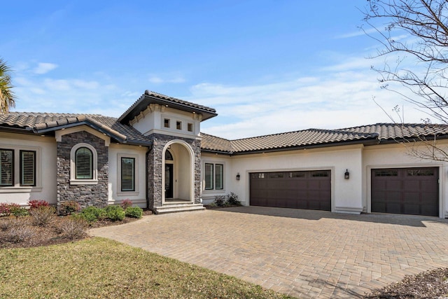 mediterranean / spanish-style home with stucco siding, decorative driveway, stone siding, a tile roof, and a garage