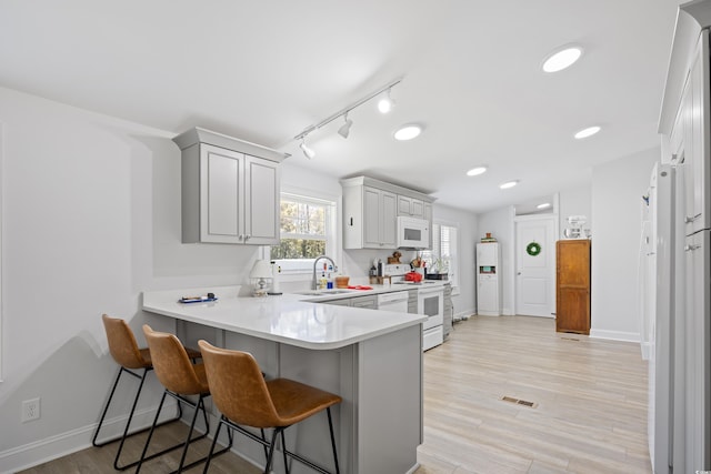 kitchen with white appliances, a sink, light countertops, light wood-style floors, and a kitchen bar