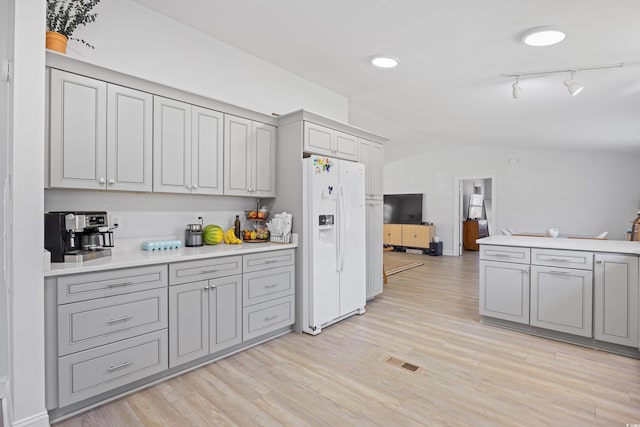 kitchen featuring lofted ceiling, light wood-style floors, white refrigerator with ice dispenser, and gray cabinetry