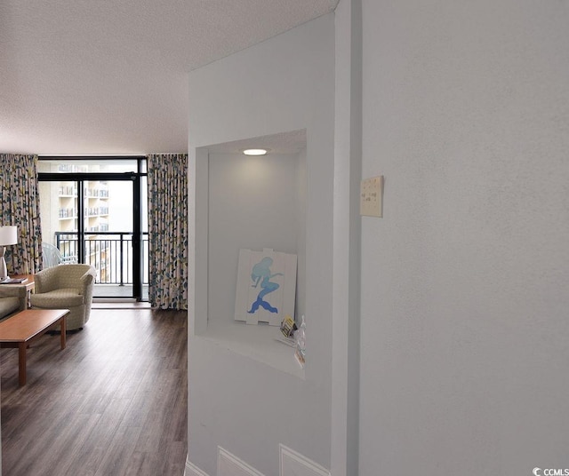 hall featuring baseboards, a wall of windows, a textured ceiling, and wood finished floors
