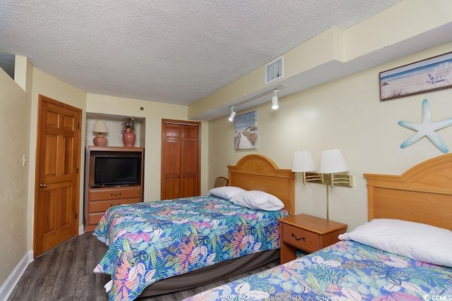 bedroom featuring a closet, wood finished floors, rail lighting, a textured ceiling, and visible vents