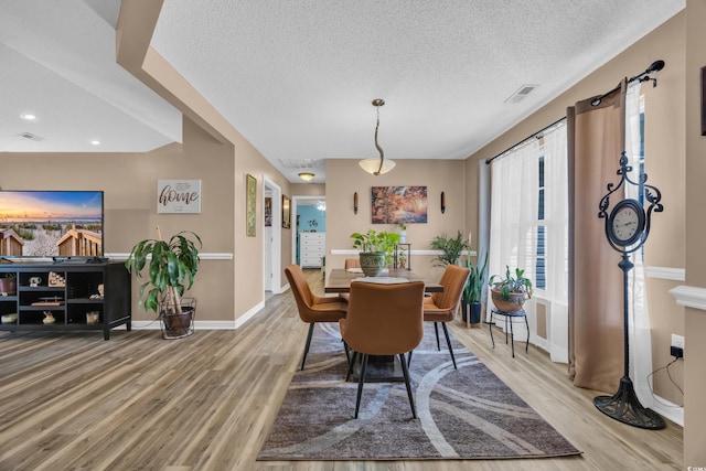 dining space with visible vents, a textured ceiling, baseboards, and wood finished floors