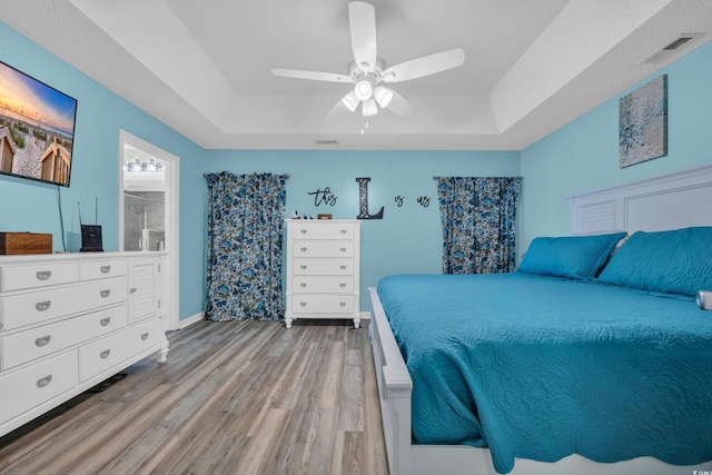 bedroom featuring baseboards, visible vents, light wood-type flooring, and a raised ceiling