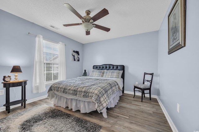 bedroom featuring baseboards, a textured ceiling, visible vents, a ceiling fan, and wood finished floors