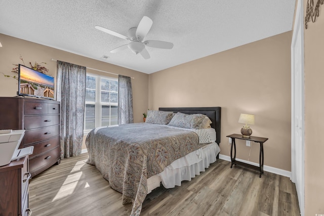 bedroom featuring light wood-style flooring, baseboards, ceiling fan, and a textured ceiling