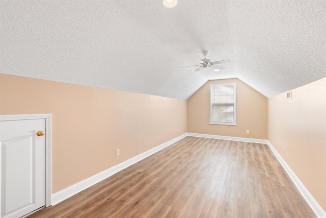 additional living space with light wood-style flooring, a textured ceiling, baseboards, lofted ceiling, and ceiling fan