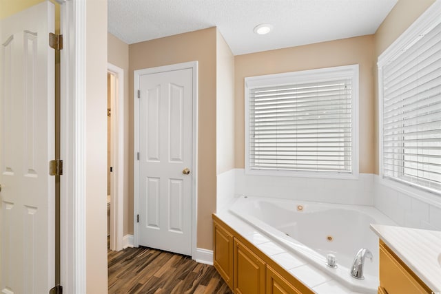 bathroom featuring vanity, wood finished floors, a tub with jets, and a textured ceiling