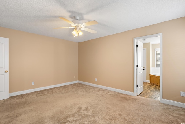 unfurnished bedroom with a textured ceiling, connected bathroom, baseboards, and light carpet
