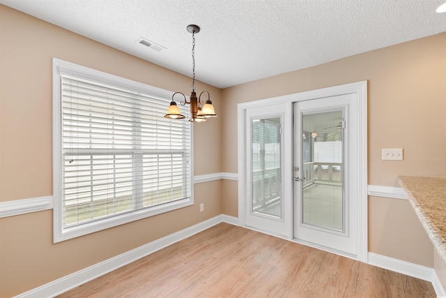 unfurnished dining area featuring light wood-type flooring, visible vents, a textured ceiling, an inviting chandelier, and baseboards