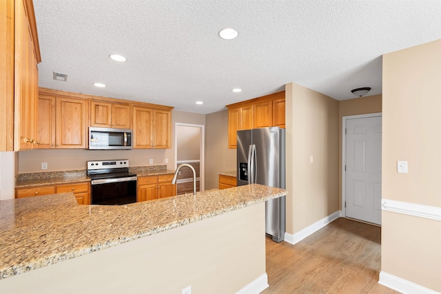 kitchen featuring light stone counters, baseboards, visible vents, light wood finished floors, and stainless steel appliances