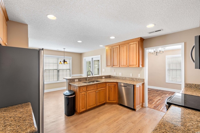 kitchen with a sink, stainless steel appliances, a peninsula, light wood finished floors, and a chandelier